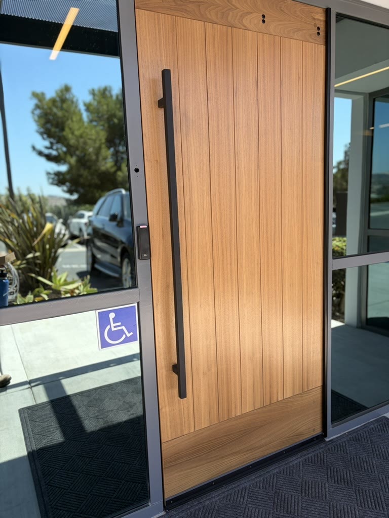Modern wood entry door with a full-height pull handle and discreet access reader on the frame
