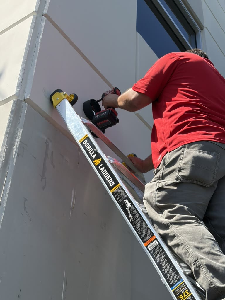 Technician on a ladder drilling a camera mount on an exterior wall